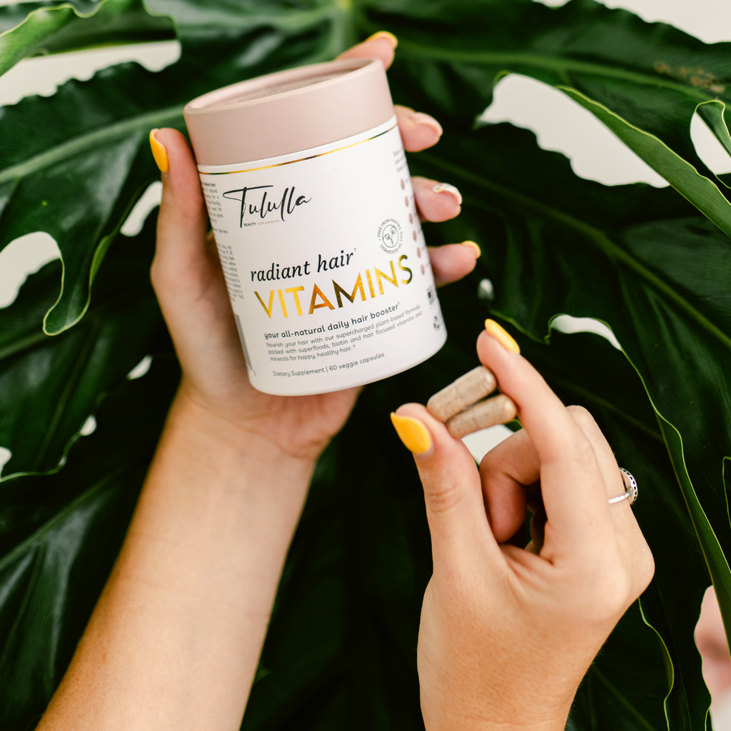 Radiant Hair Vitamins plastic free packaging and 2 vegan-friendly capsules in the hands of a beautiful model.
